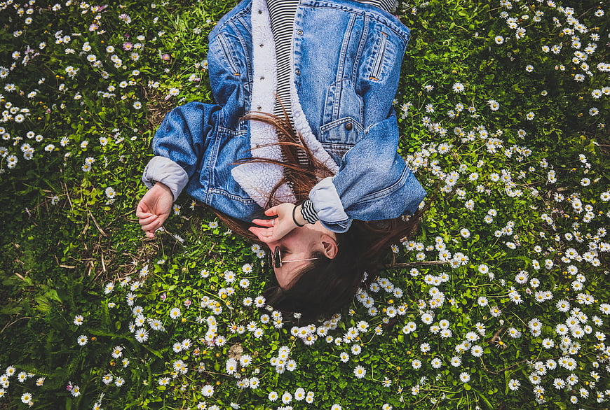 Woman in denim jacket lying in field of daisies