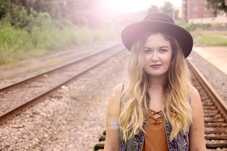 Blonde woman in hat standing on railroad tracks