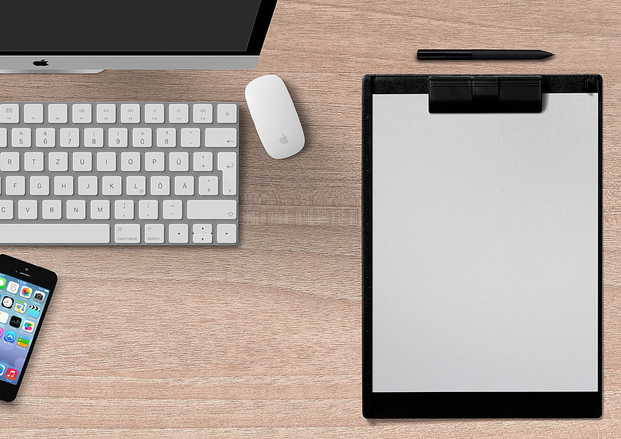 Top-Down Office Desk Setup With Clipboard, Keyboard, Mouse, And Smartphone