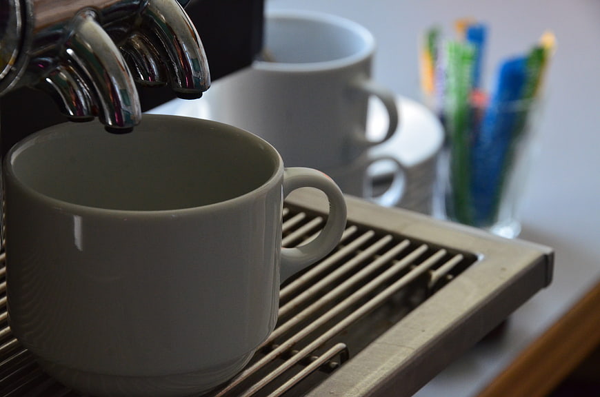 White ceramic coffee cup under espresso machine spouts