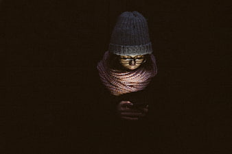 Woman in winter hat and scarf looking at phone in dark