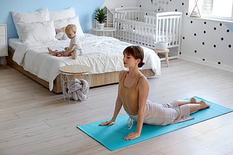 Mother doing yoga in bedroom while baby plays on bed