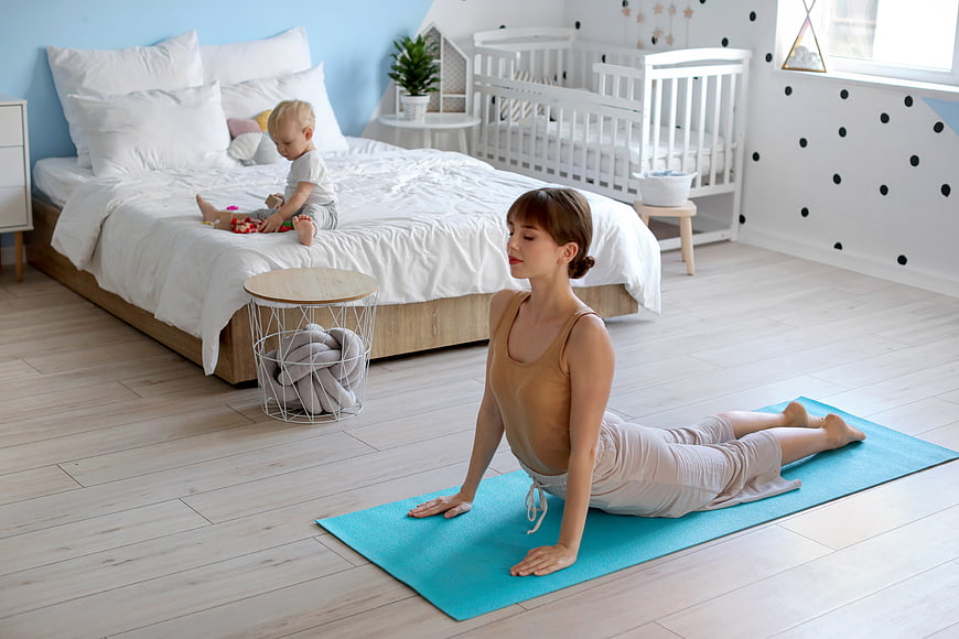 Mother doing yoga in bedroom while baby plays on bed