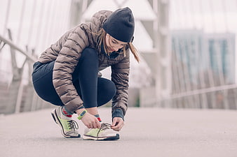 Woman tying running shoes on urban bridge