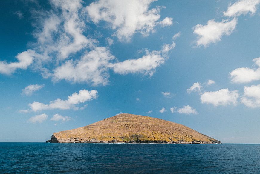Solitary grassy island in blue ocean under cloudy sky