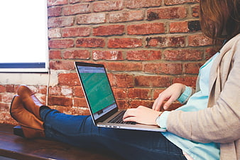Woman working on laptop against exposed brick wall