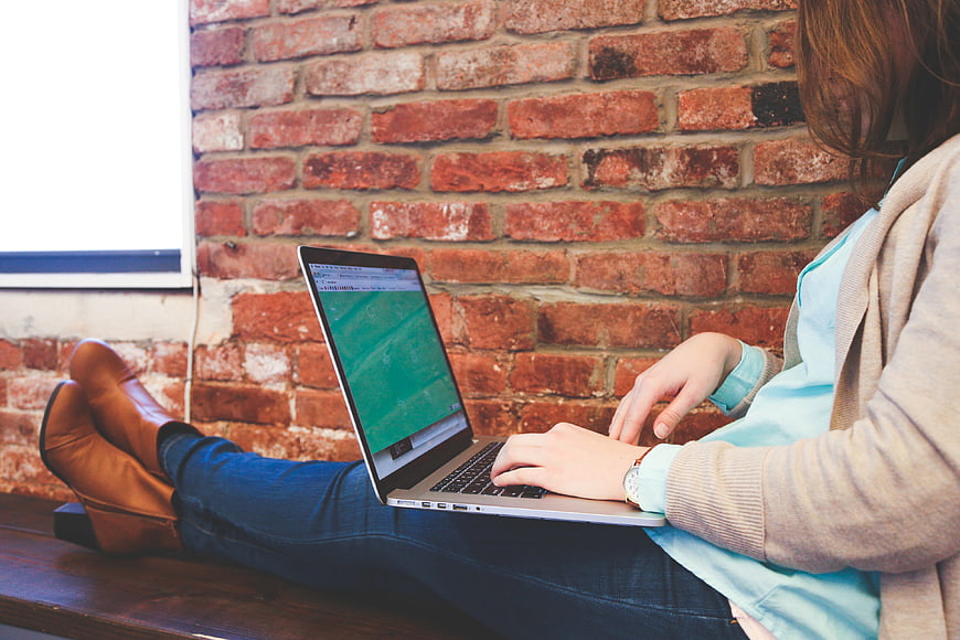 Woman working on laptop against exposed brick wall