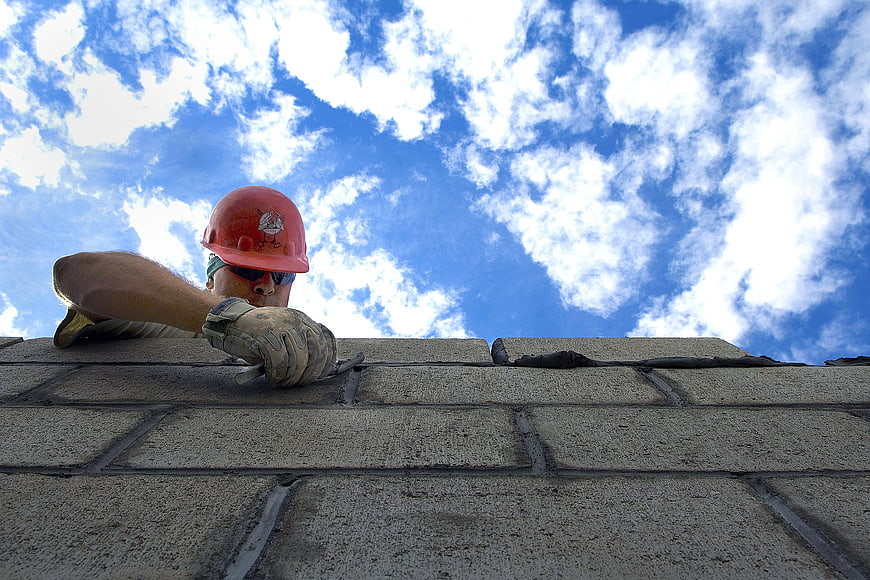 Construction worker laying bricks against blue sky
