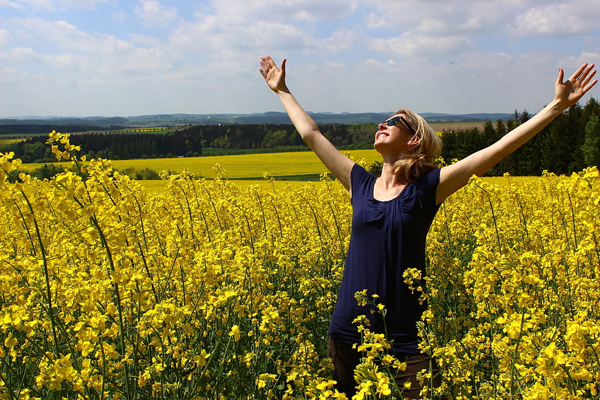 Happy woman with arms raised in yellow rapeseed field