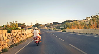 Man Riding Red Moped on Rural Road at Sunset