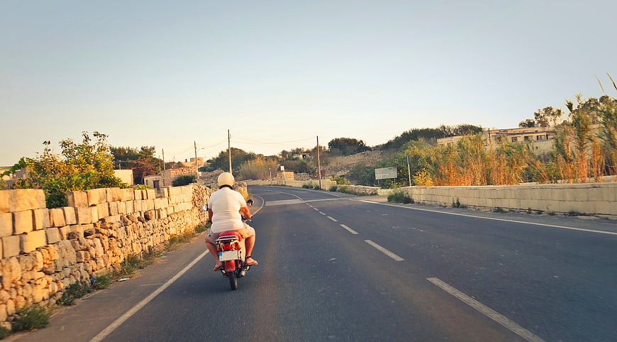 Man Riding Red Moped on Rural Road at Sunset