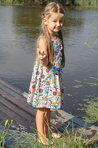 Cute little girl in floral dress standing on wooden dock by lake