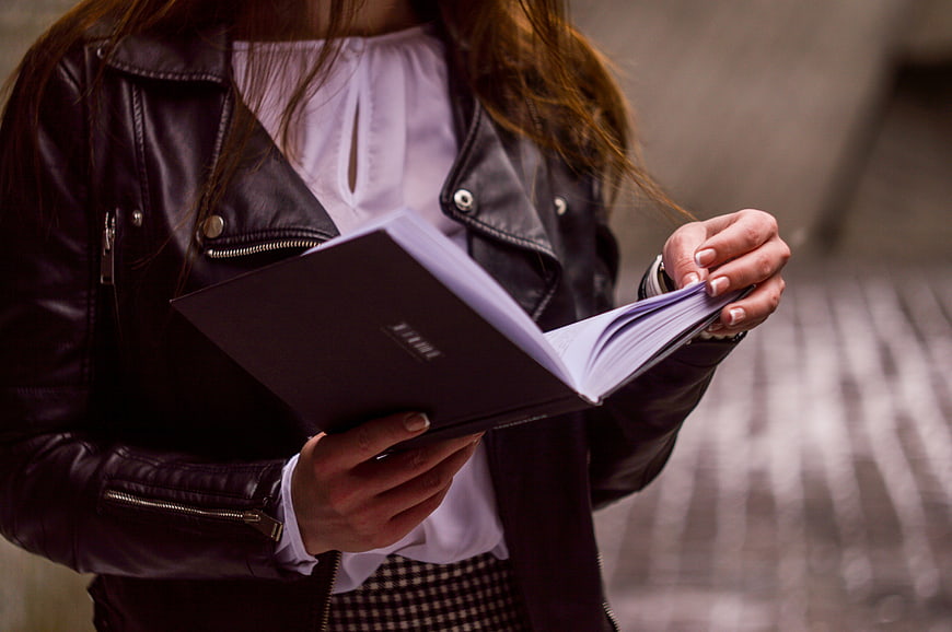 Woman in leather jacket reading a book outdoors