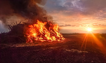 Large bonfire burning in field at sunset with smoke