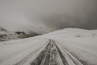 Snowy winter road winding through mountains under dark storm clouds