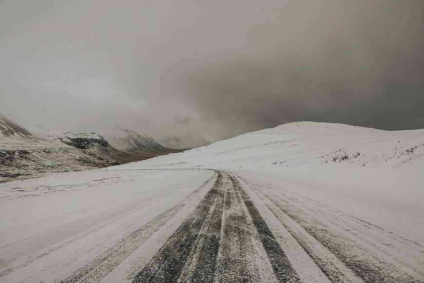 Snowy winter road winding through mountains under dark storm clouds