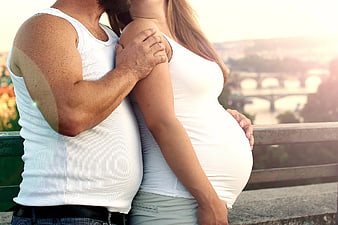 Pregnant couple embracing with city bridge background
