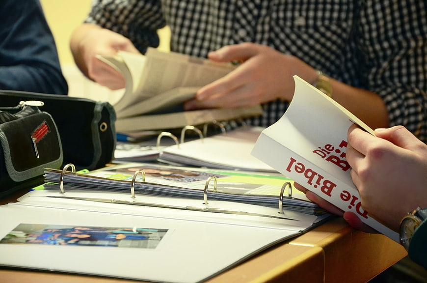Close-up of hands holding a German Bible and binders