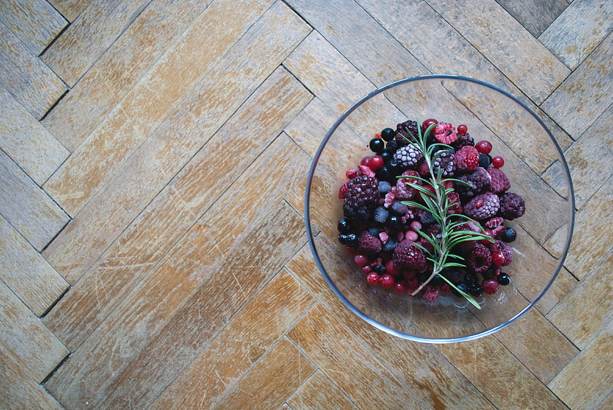 Top view of frozen mixed berries in glass bowl on wood