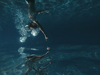 Underwater shot of man diving with reflection in water