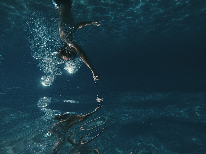 Underwater shot of man diving with reflection in water