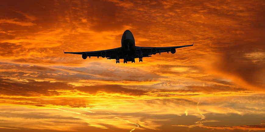 Silhouette of a commercial airplane landing against a vibrant orange sunset sky