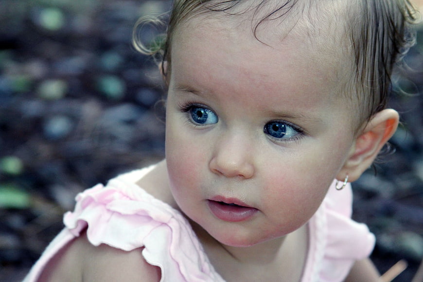 Close-up portrait of a baby girl with blue eyes and pink dress
