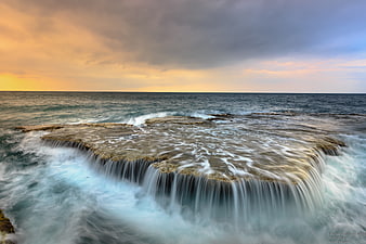 Dramatic Ocean Waterfall Flowing Over Rocks at Sunset