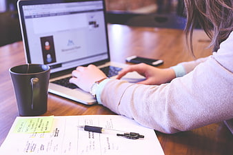 Woman typing on laptop with notes and coffee at desk