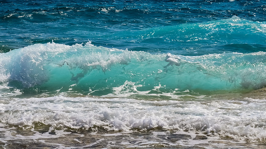 Turquoise ocean wave crashing on sandy beach