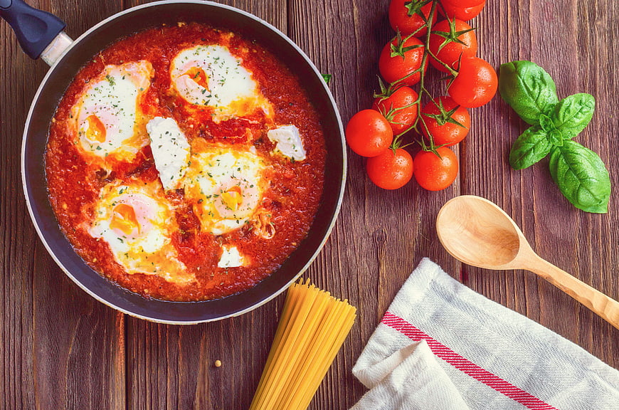 Shakshuka with Eggs in Pan on Wooden Table