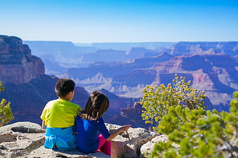 Two children sitting on a cliff edge overlooking the Grand Canyon