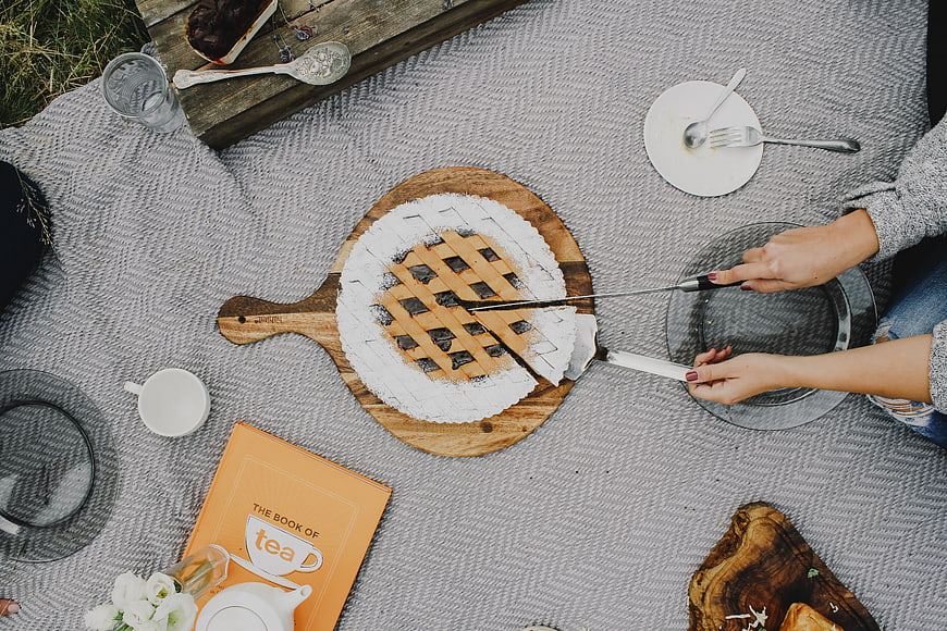 Top view of hands cutting lattice pie on picnic blanket