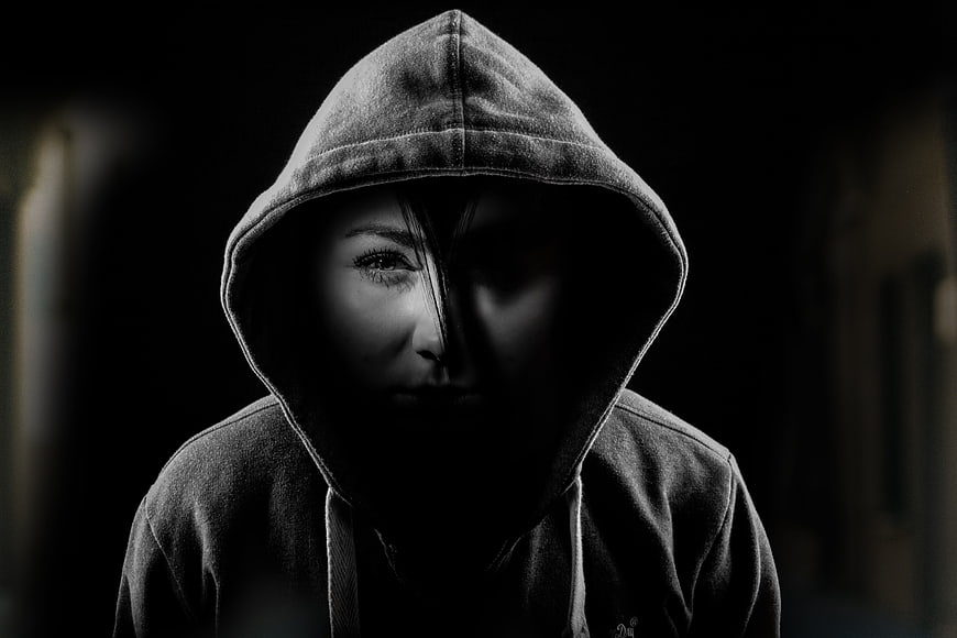 Mysterious woman in dark hoodie with split face lighting