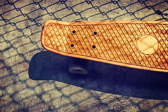 Vintage Orange Skateboard on Concrete with Chain Link Shadows