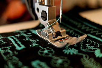 Close-up of sewing machine presser foot stitching teal thread on black fabric