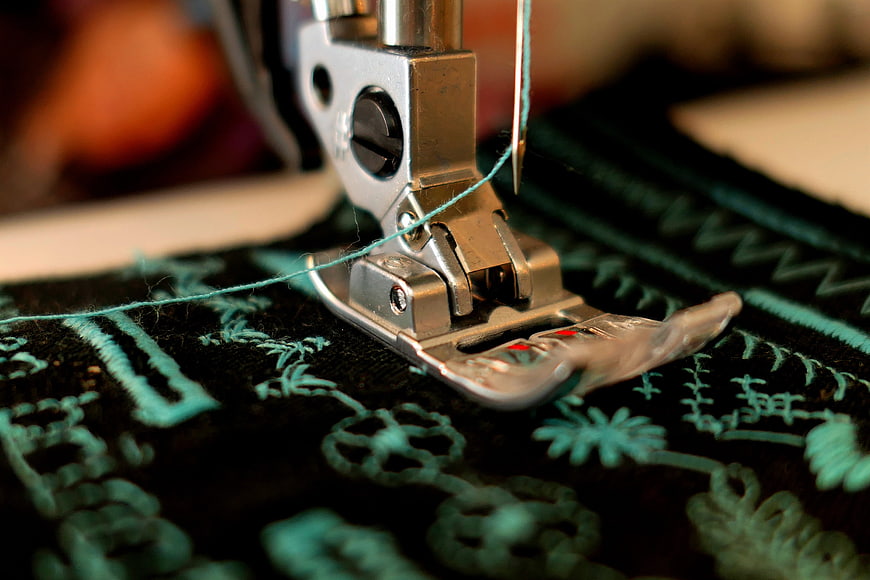 Close-up of sewing machine presser foot stitching teal thread on black fabric