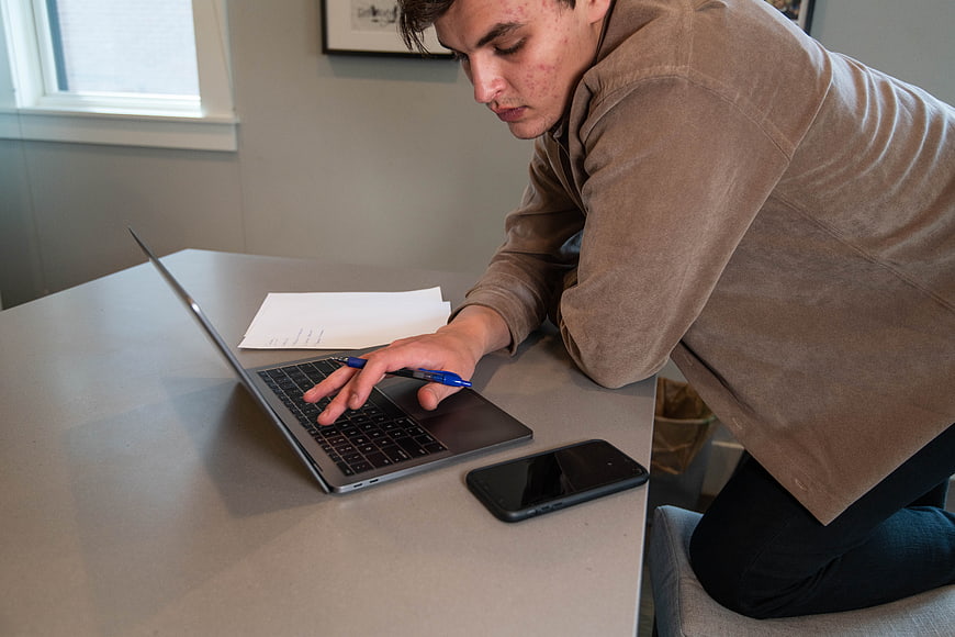 Young man working on laptop at desk with smartphone