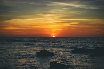 Sunset over ocean with silhouetted rocks and waves