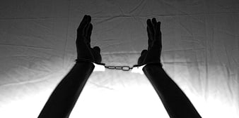 Silhouette of handcuffed hands raised against white background