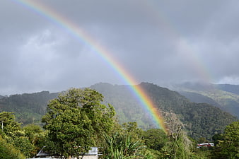 Vibrant Rainbow Arching Over Lush Green Mountain Landscape