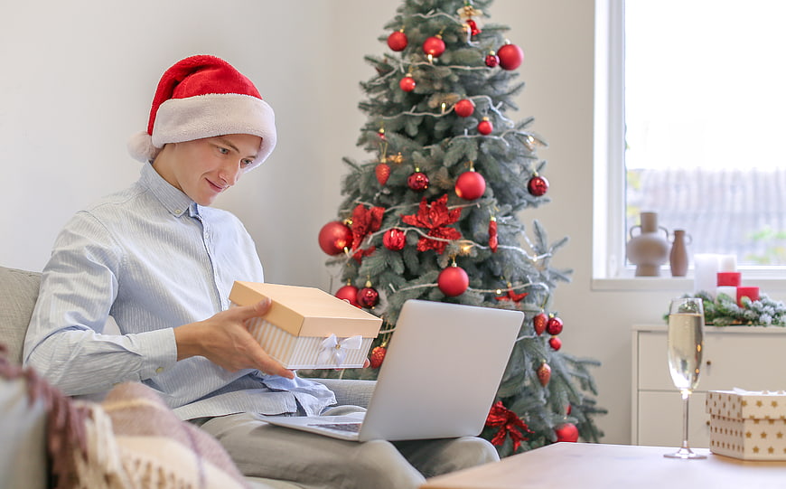 Man in Santa Hat Opening Gift with Laptop and Christmas Tree