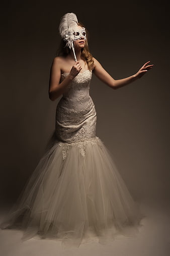 Elegant woman in white gown holding feathered masquerade mask