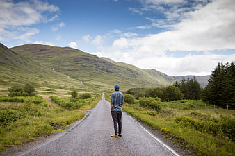 Man Standing on Rural Road Facing Green Mountains