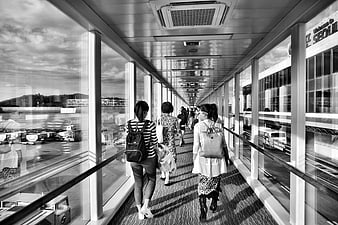 Travelers walking through airport jet bridge in black and white