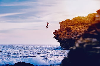 Man cliff diving into the ocean at sunset