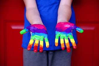 Child's Hands Covered In Rainbow Paint Against Red Background