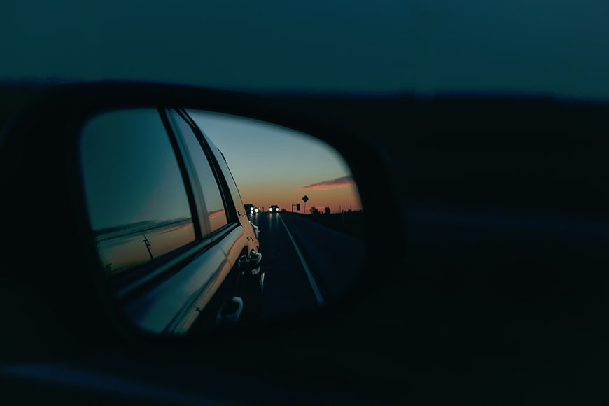 Car side mirror reflecting sunset highway drive