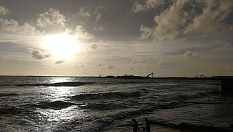 Silhouetted Figures on Beach with Construction Cranes at Sunset
