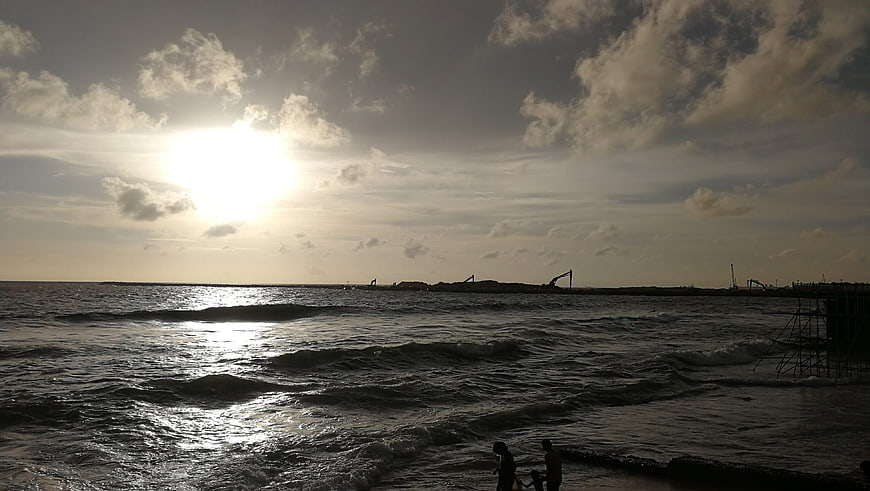 Silhouetted Figures on Beach with Construction Cranes at Sunset